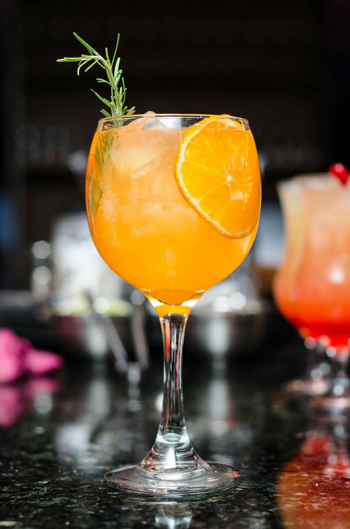 Orange cocktail in a stemmed glass, garnished with orange slice and rosemary.
