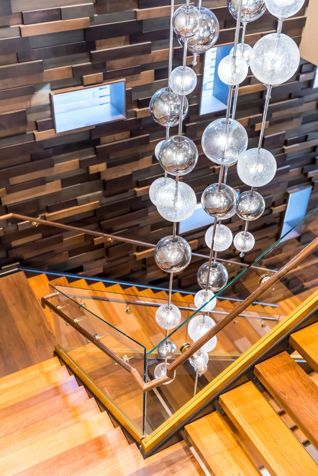 Interior staircase with glass railing and hanging globe chandelier in a modern lobby at The Walkway, which offers apartments near downtown Minneapolis.