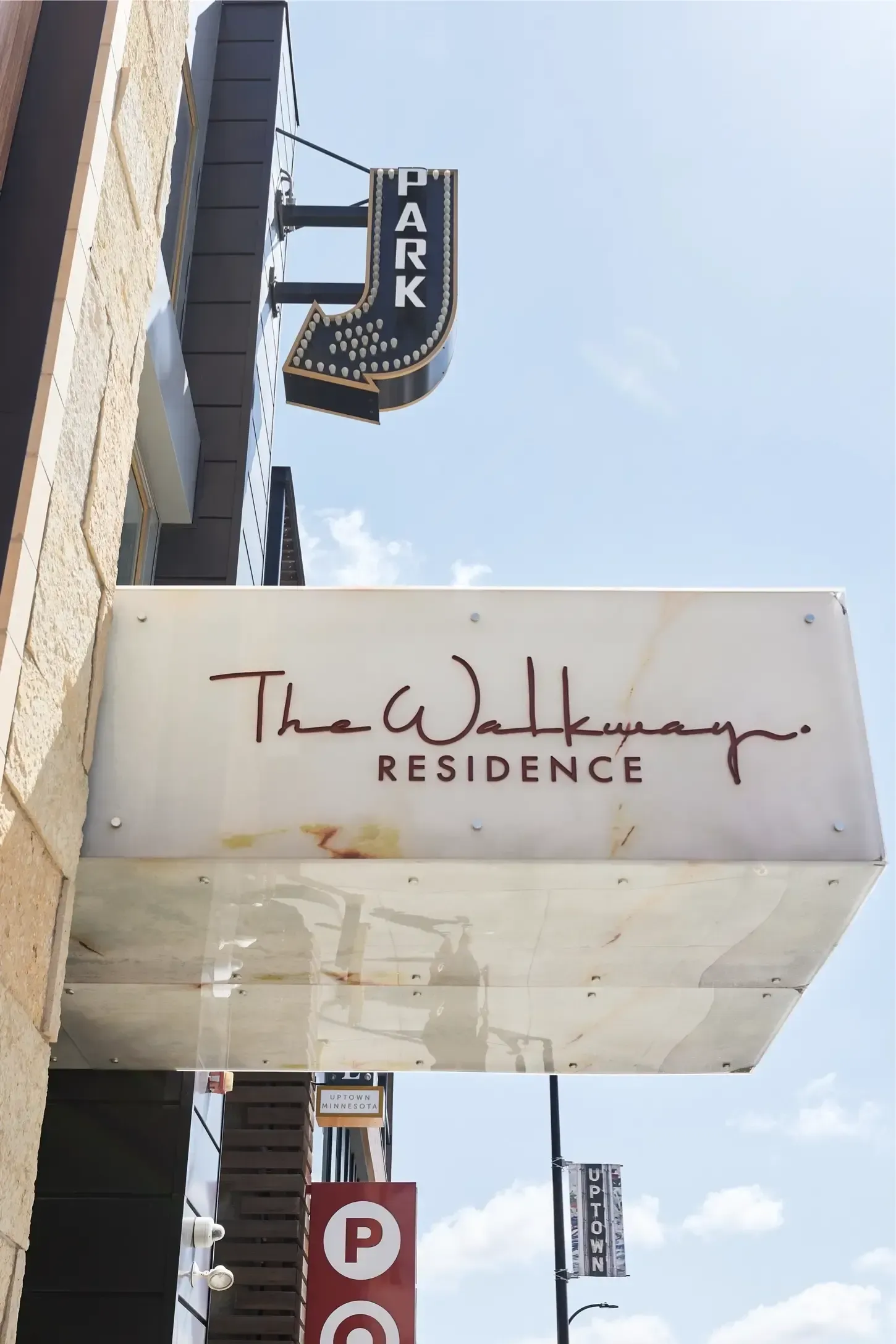 Exterior view of The Walkway Residence sign on a building with a vertical PARK sign and blue sky at The Walkway, which offers pet-friendly apartments in Minneapolis, MN.