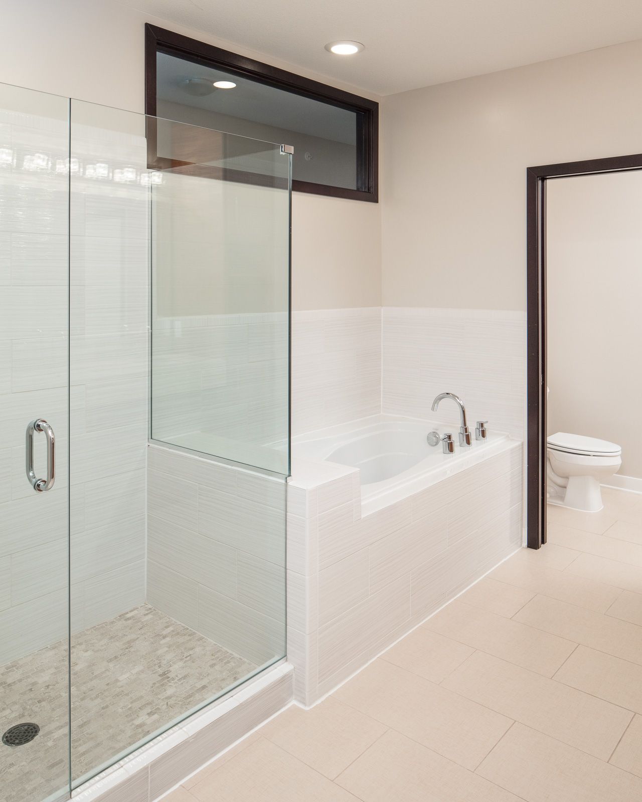 Modern apartment bathroom with glass shower enclosure, built-in tub, and adjacent toilet at The Walkway, which offers Uptown apartments in Minneapolis, MN.