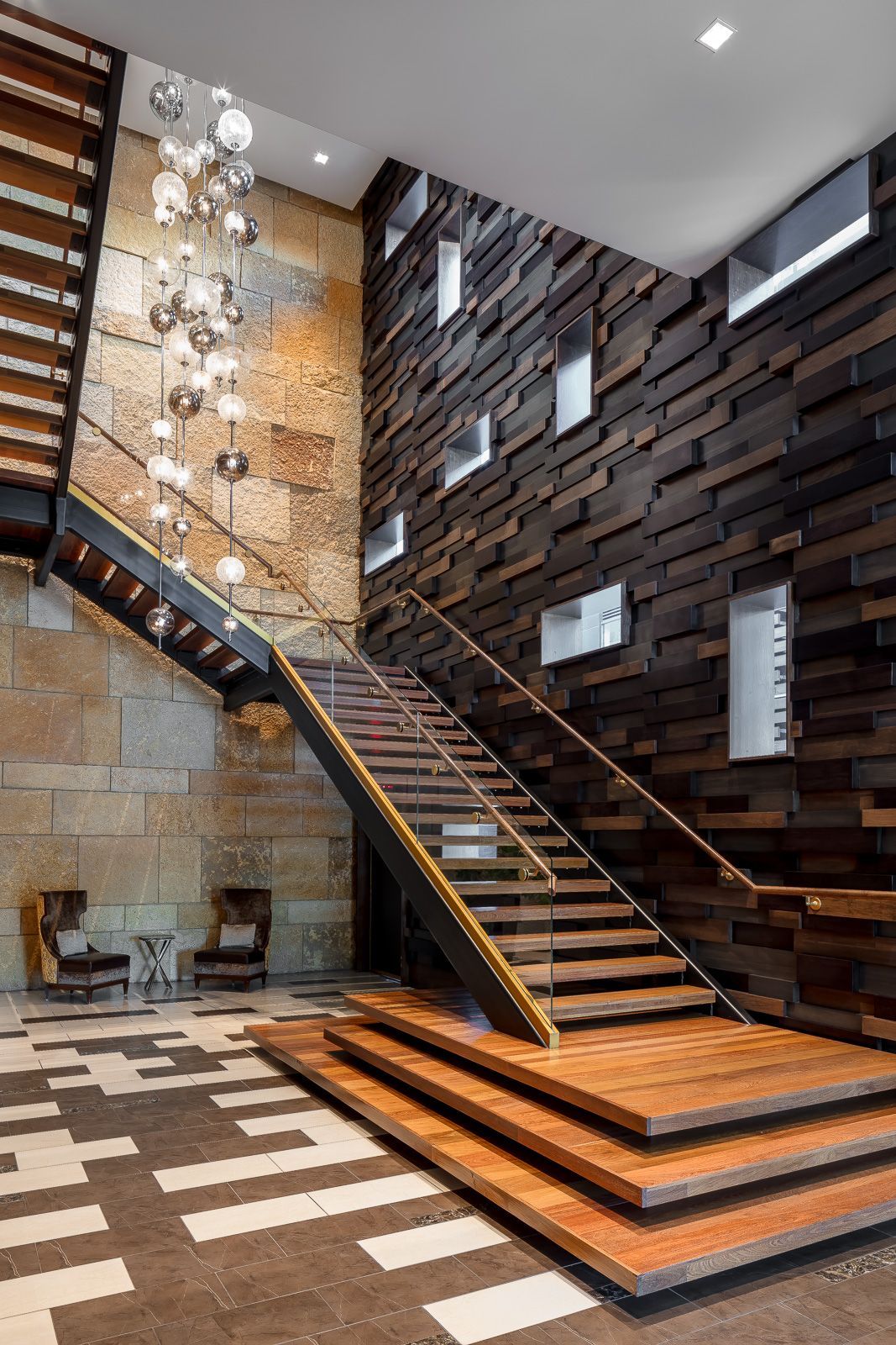 Two-story lobby with a wooden staircase, glass railings, and a hanging globe chandelier at The Walkway, which offers apartments near downtown Minneapolis.