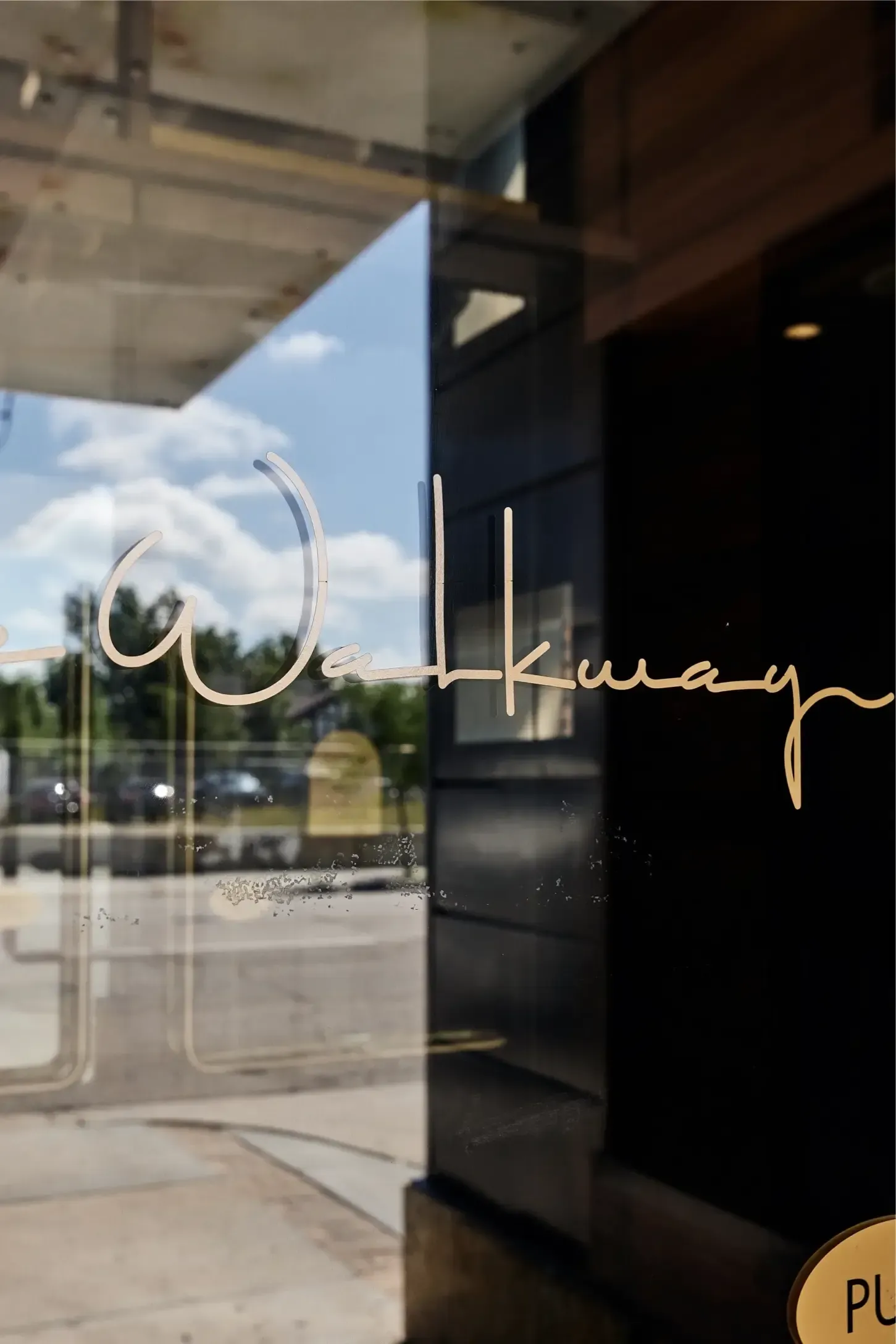 Glass entrance door with cursive sign, reflecting street outside at The Walkway, which offers Minneapolis apartments for rent.