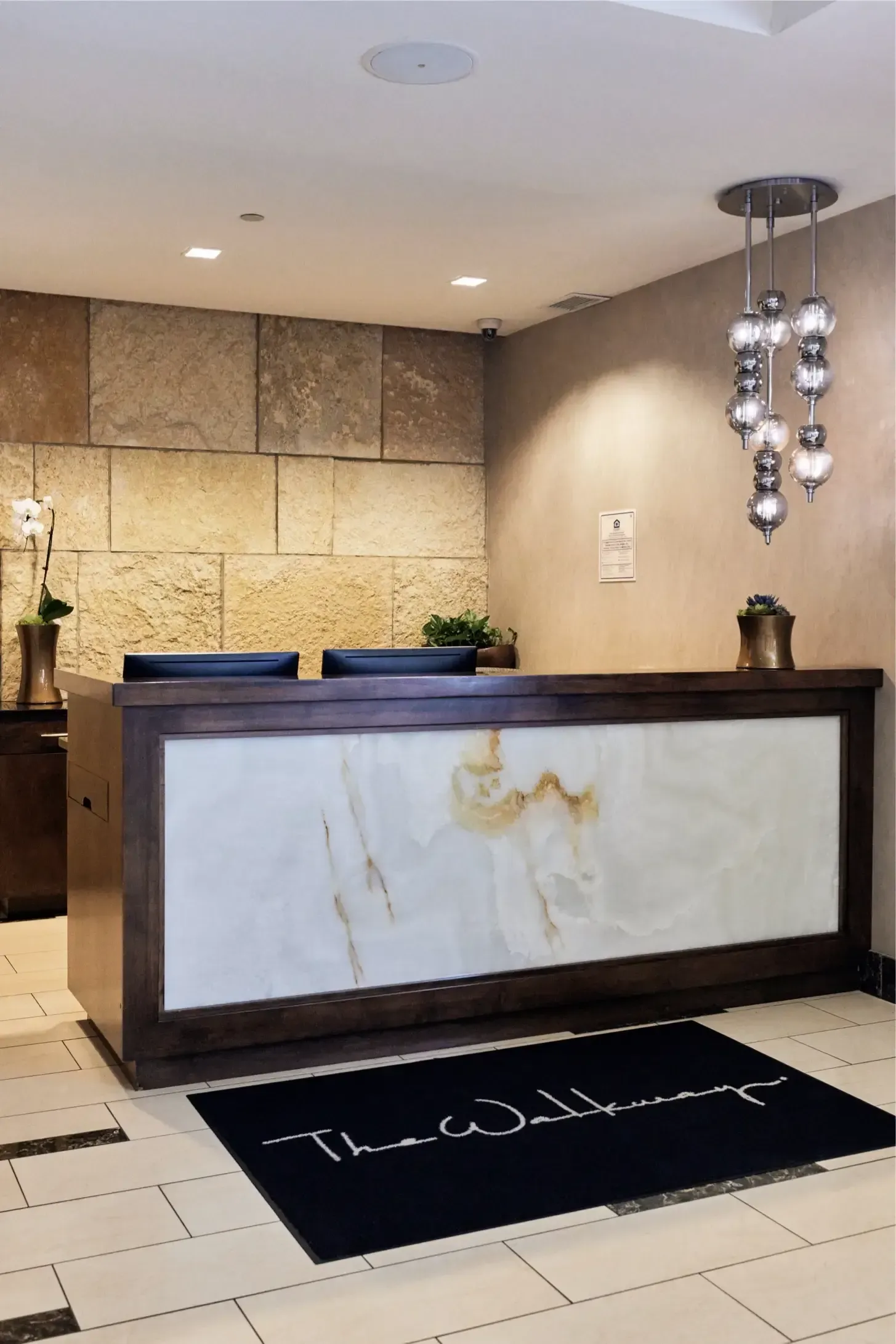 Lobby reception desk with a marble panel, stone wall, and hanging pendant lights at The Walkway, which offers Minneapolis apartments for rent.