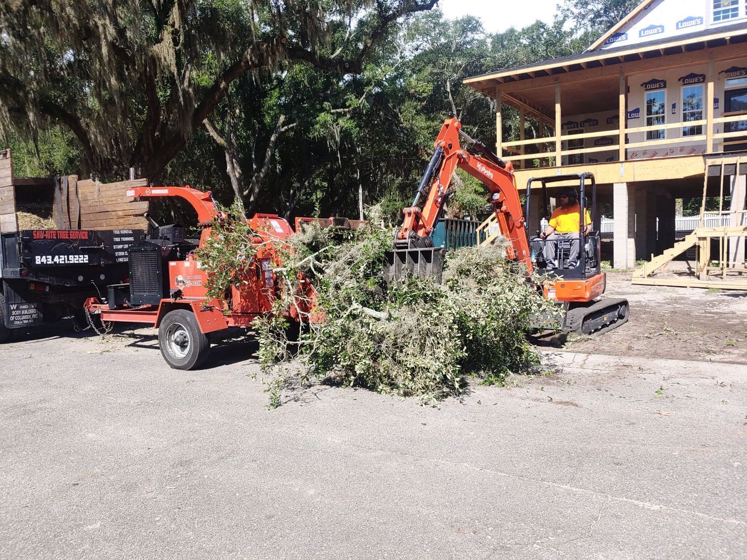 An excavator and a tree chipper are parked in front of a house under construction.