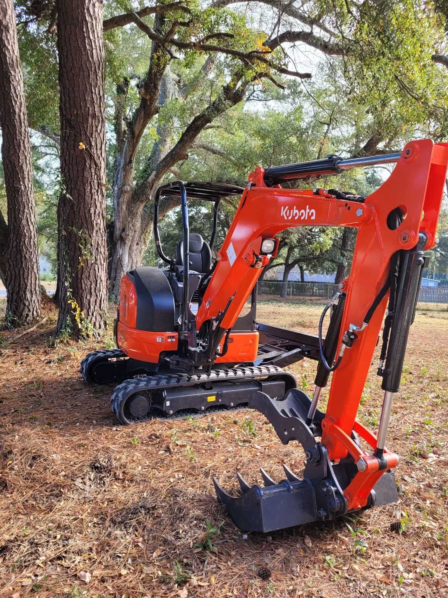 A small orange excavator is parked in a field next to trees.
