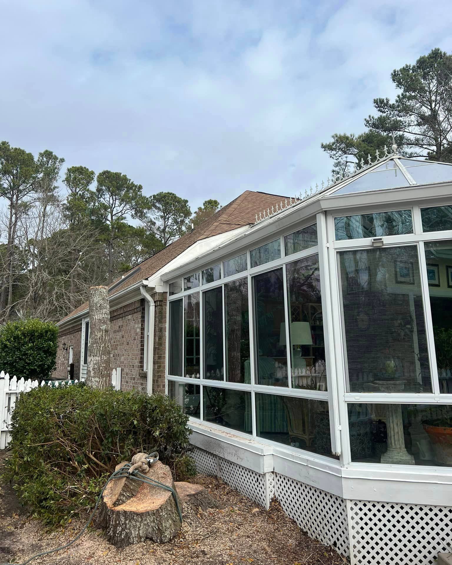 A house with a sunroom and a tree stump in front of it.