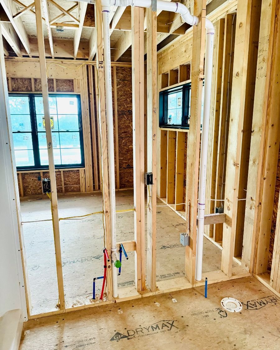 Unfinished house interior with exposed wooden framing, window, and plumbing lines on the floor.