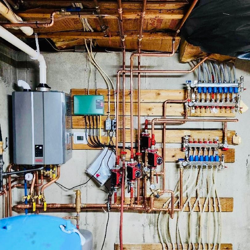 Home mechanical room with water heater, boiler, and plumbing manifolds on a basement wall