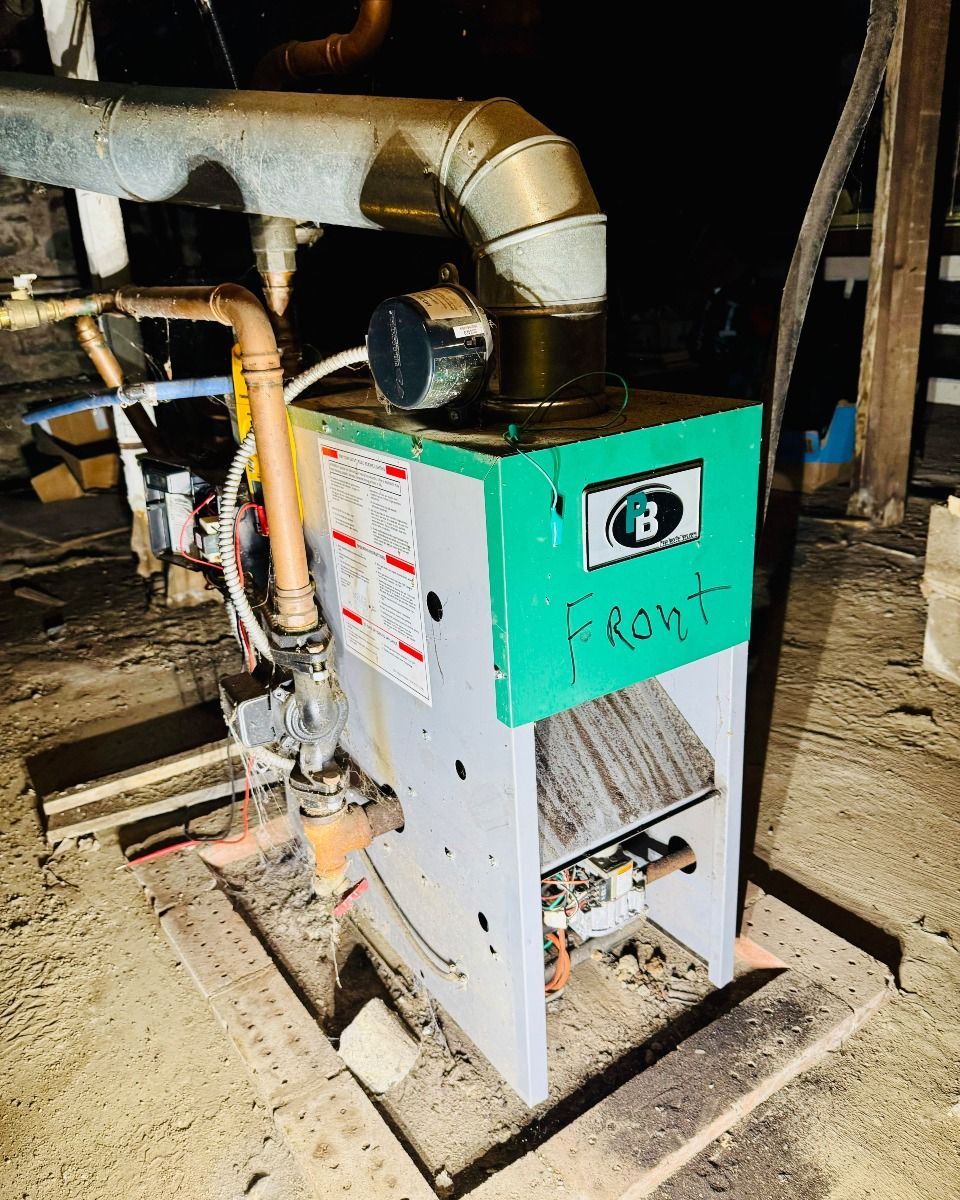 Green-and-white industrial furnace with ductwork in a dusty utility room