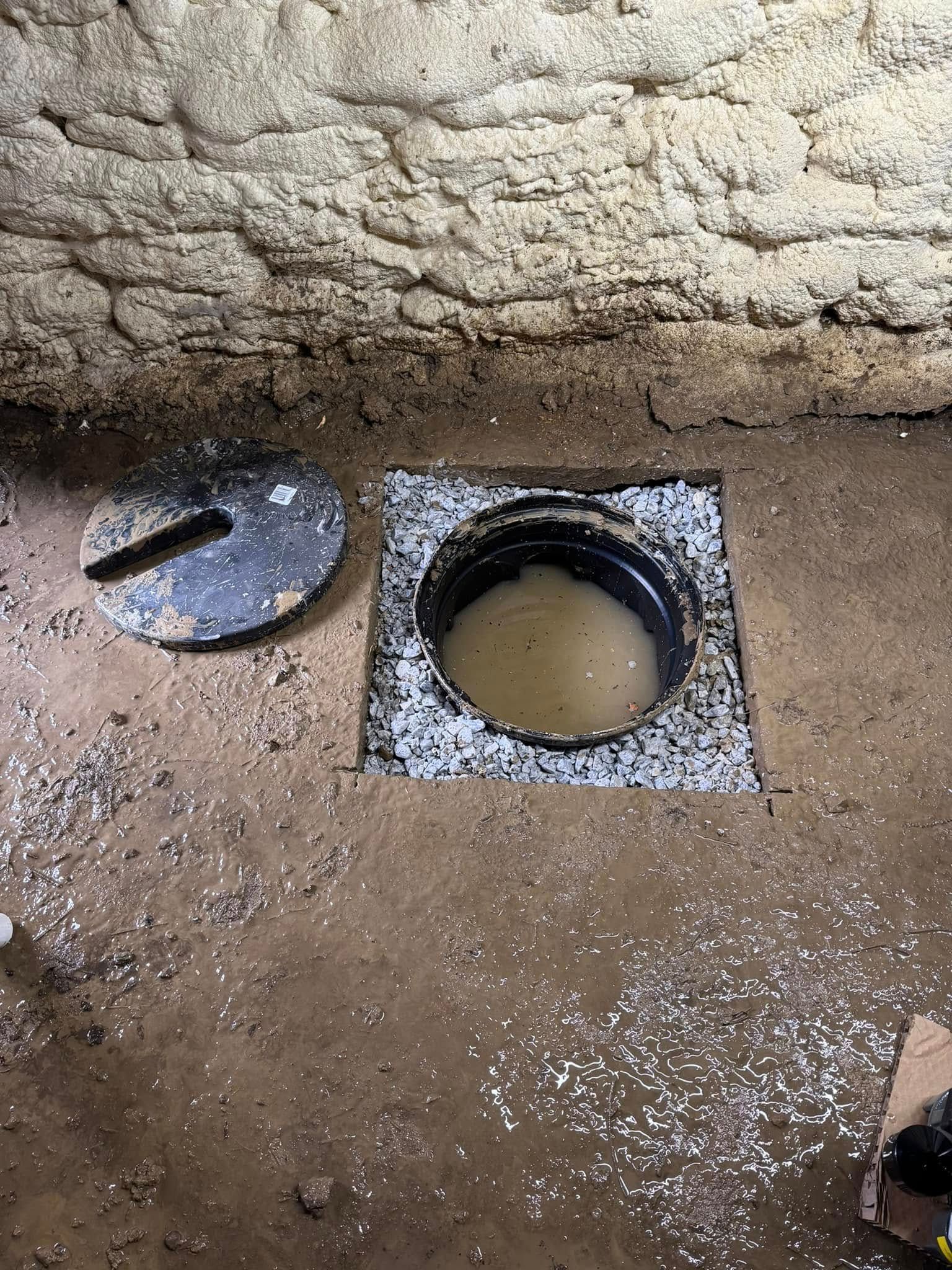 Open ground pit with a round lid beside it, set against an earthen wall.