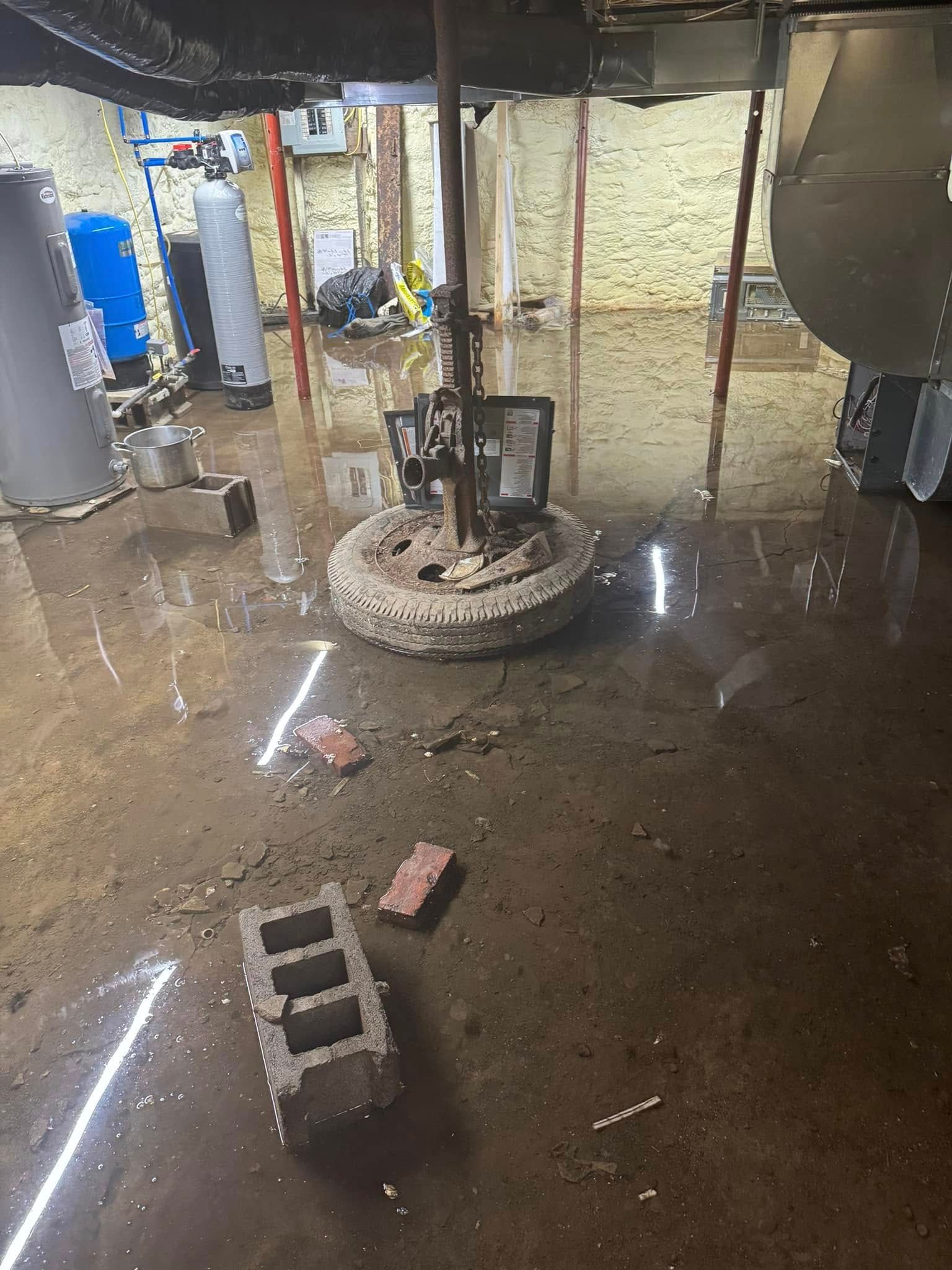 Flooded basement with standing water, cinder blocks, a brick, and a central metal structure under exposed beams