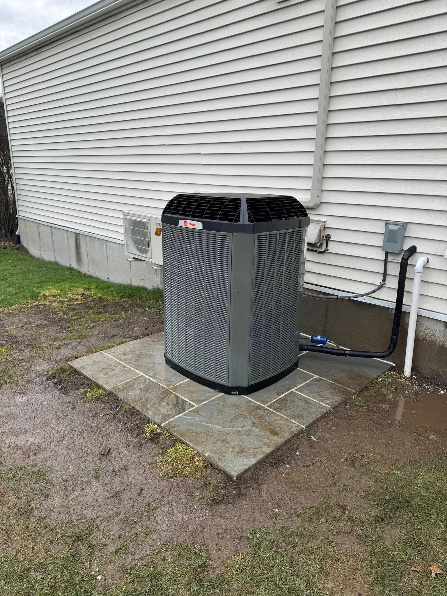 Outdoor air conditioner unit beside a house, on a concrete pad near a vinyl-sided wall