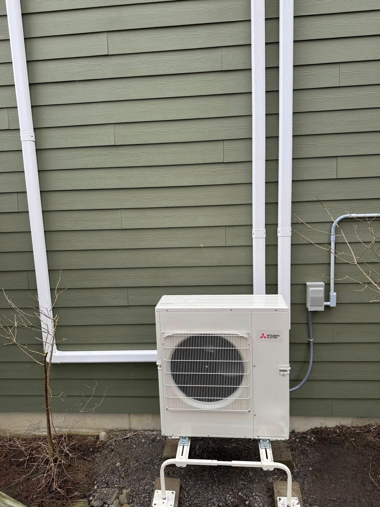 Outdoor air conditioner unit against a green house wall with white conduit and piping
