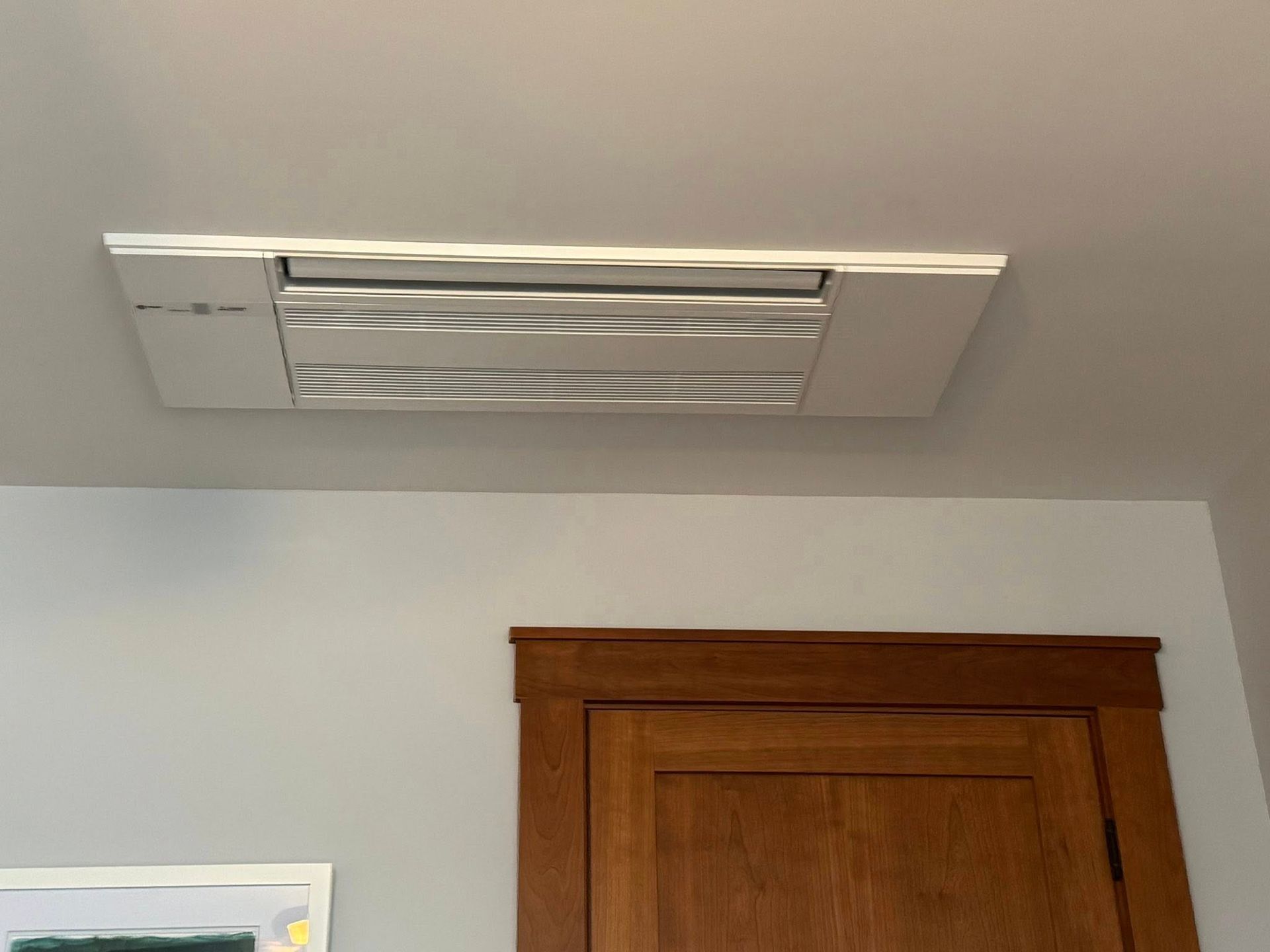 White ceiling vent above a wooden cabinet in a light gray room