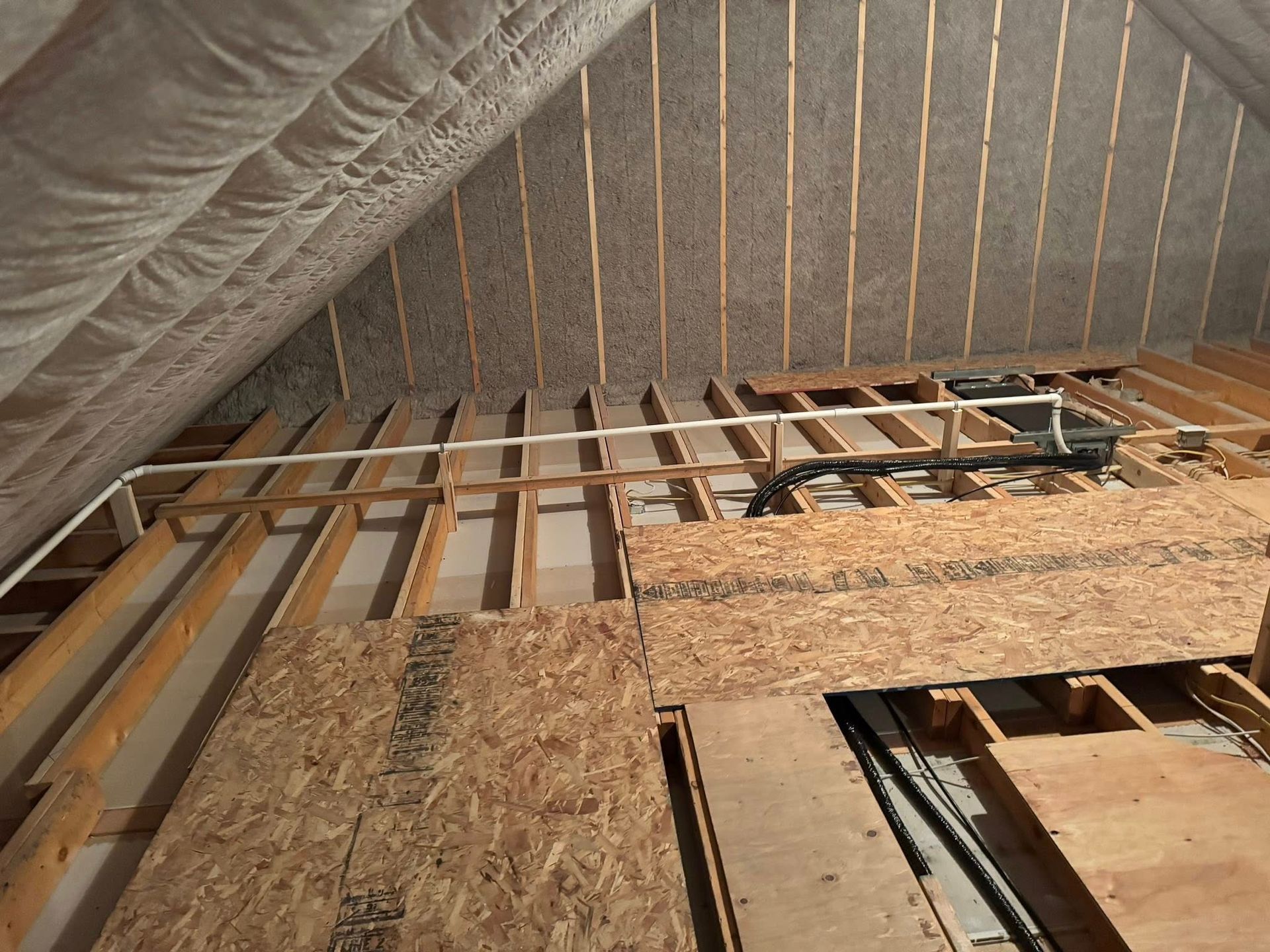 Insulated attic framing with exposed wooden joists and plywood subflooring under a sloped roof