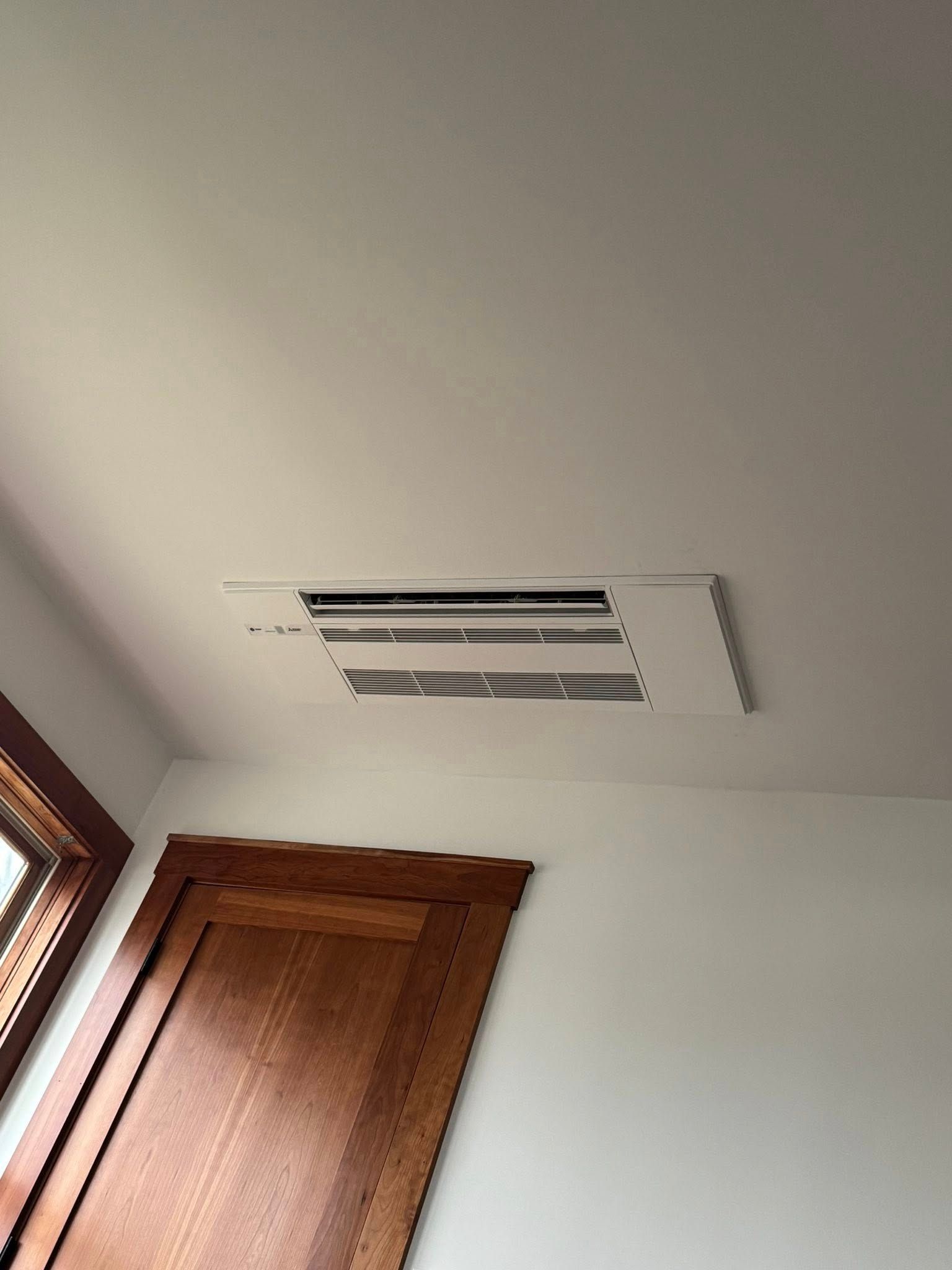 Ceiling vent on white ceiling beside a wooden door and window frame