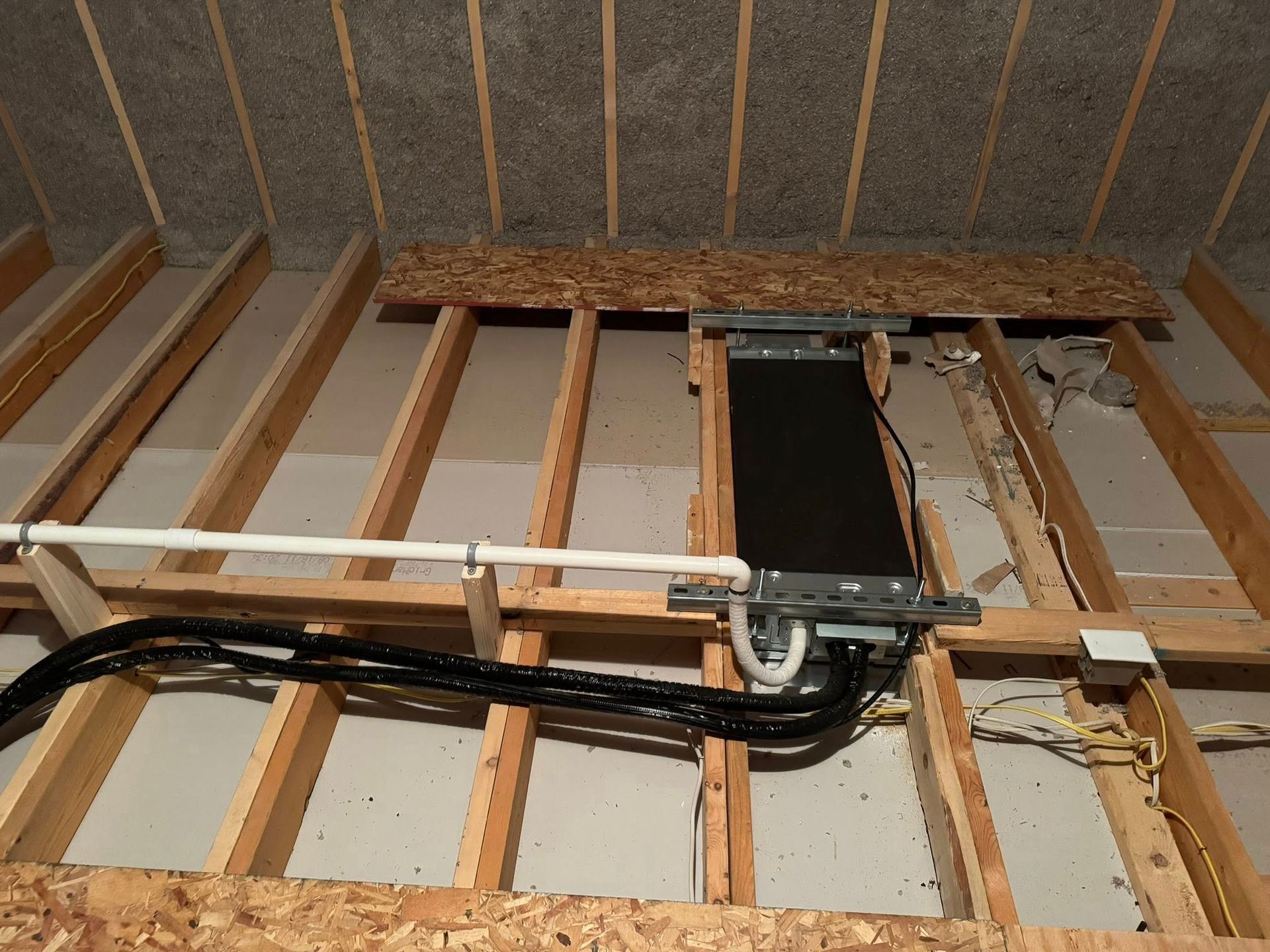 Partially framed ceiling with exposed wooden joists, insulation, and black utility pipes