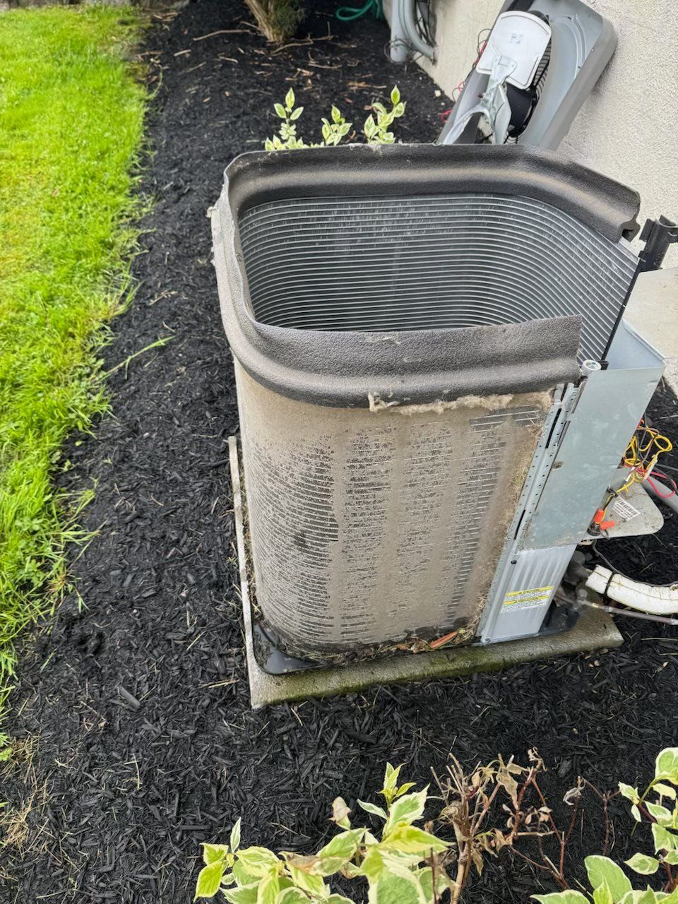 Outdoor HVAC unit with dirty, bent top grille beside a lawn and mulch bed