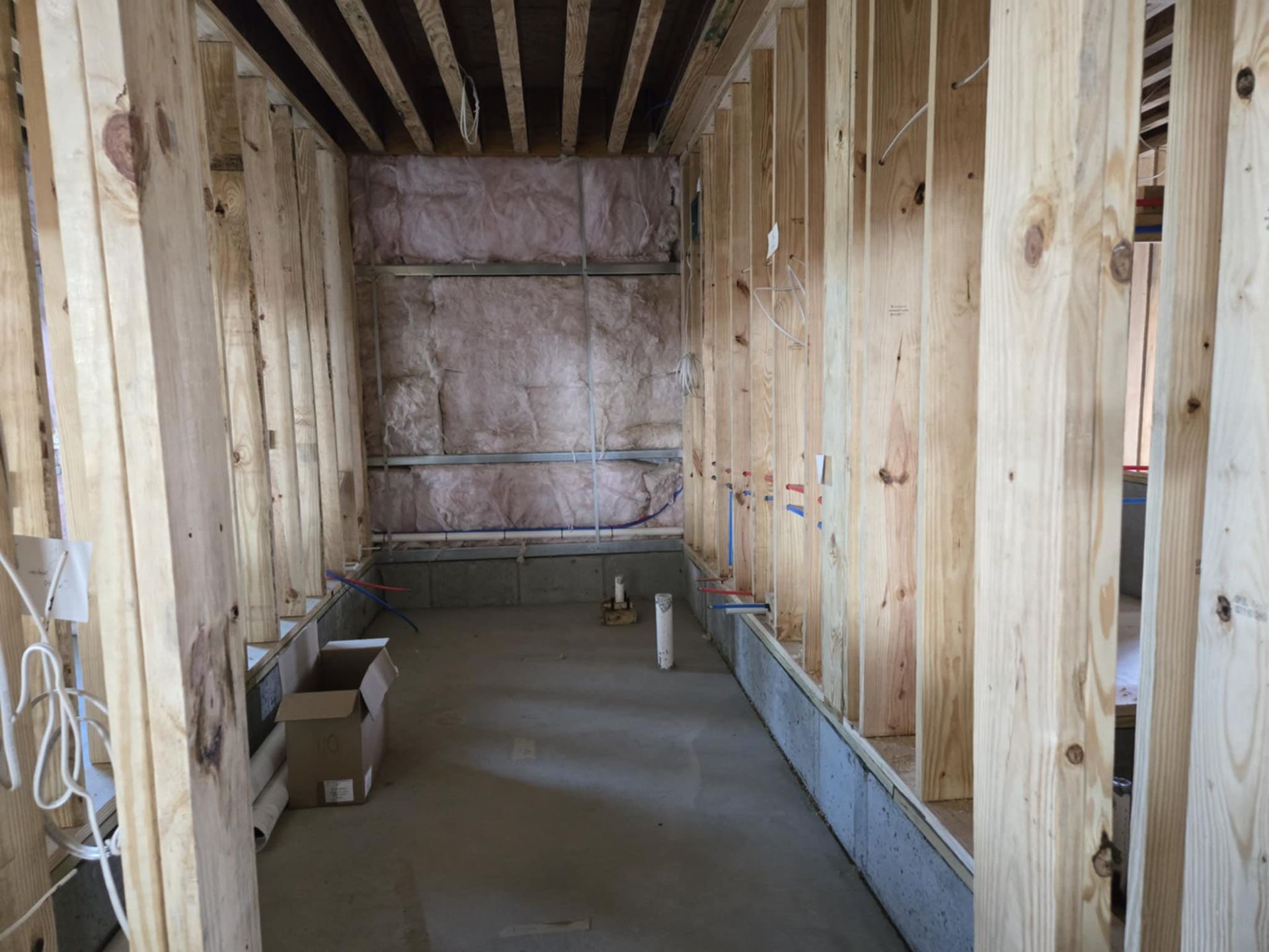 Unfinished interior with exposed wood framing, insulation, and a concrete floor under construction.