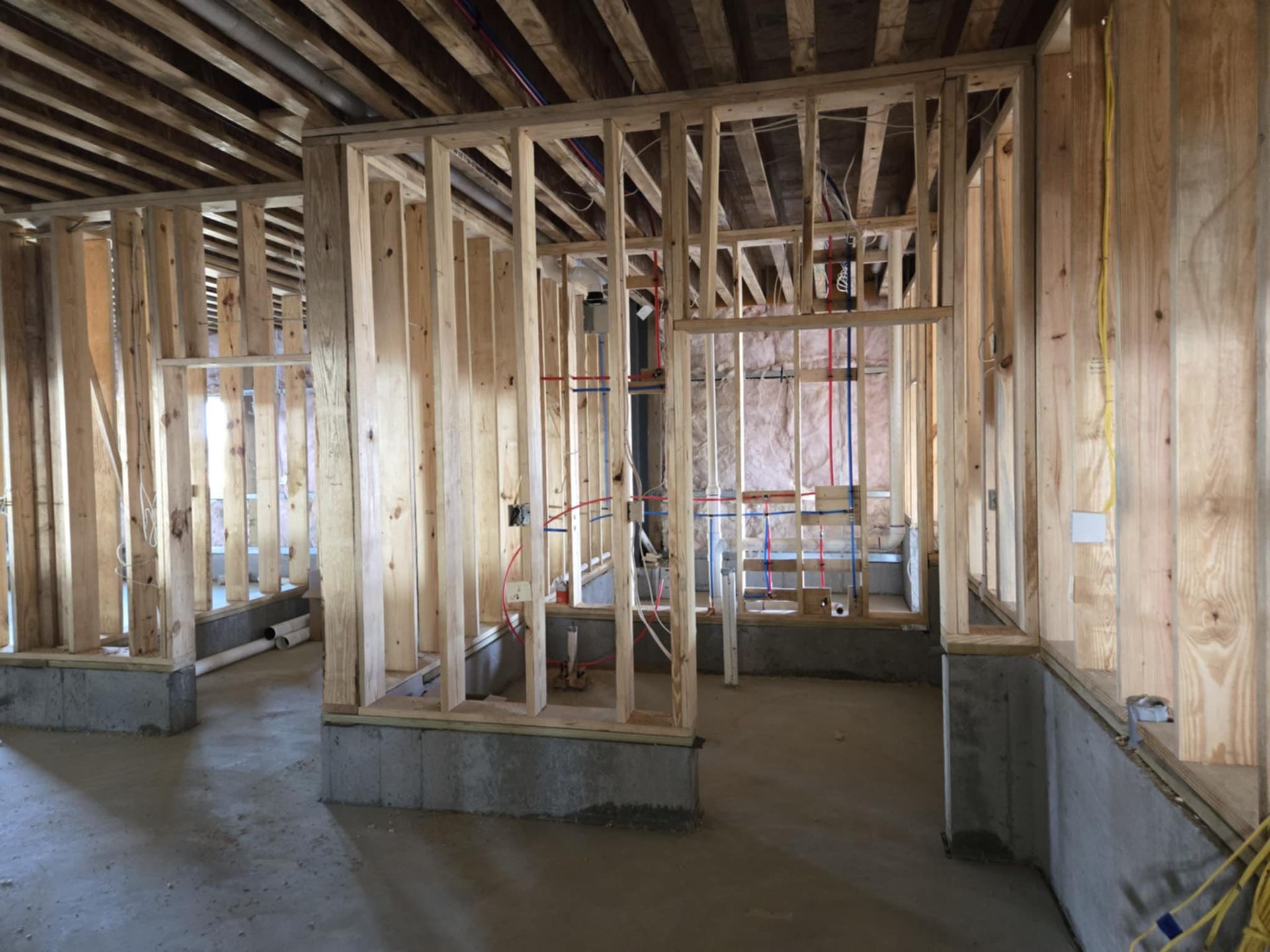Unfinished house interior with exposed wooden framing, concrete floor, and open window and door spaces