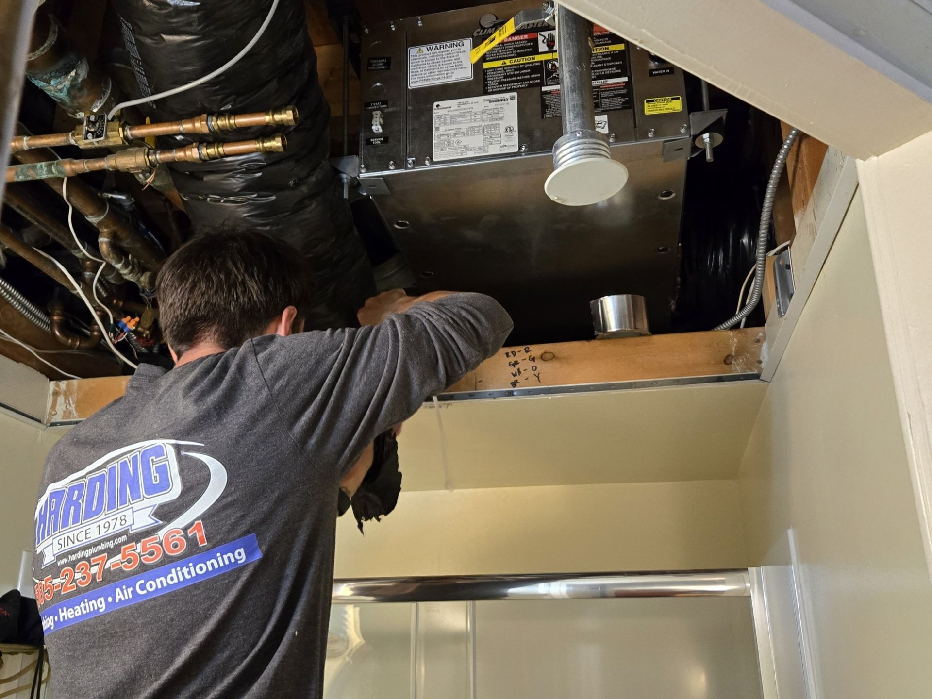 Technician working on exposed ceiling ductwork and wiring above a hallway or room opening