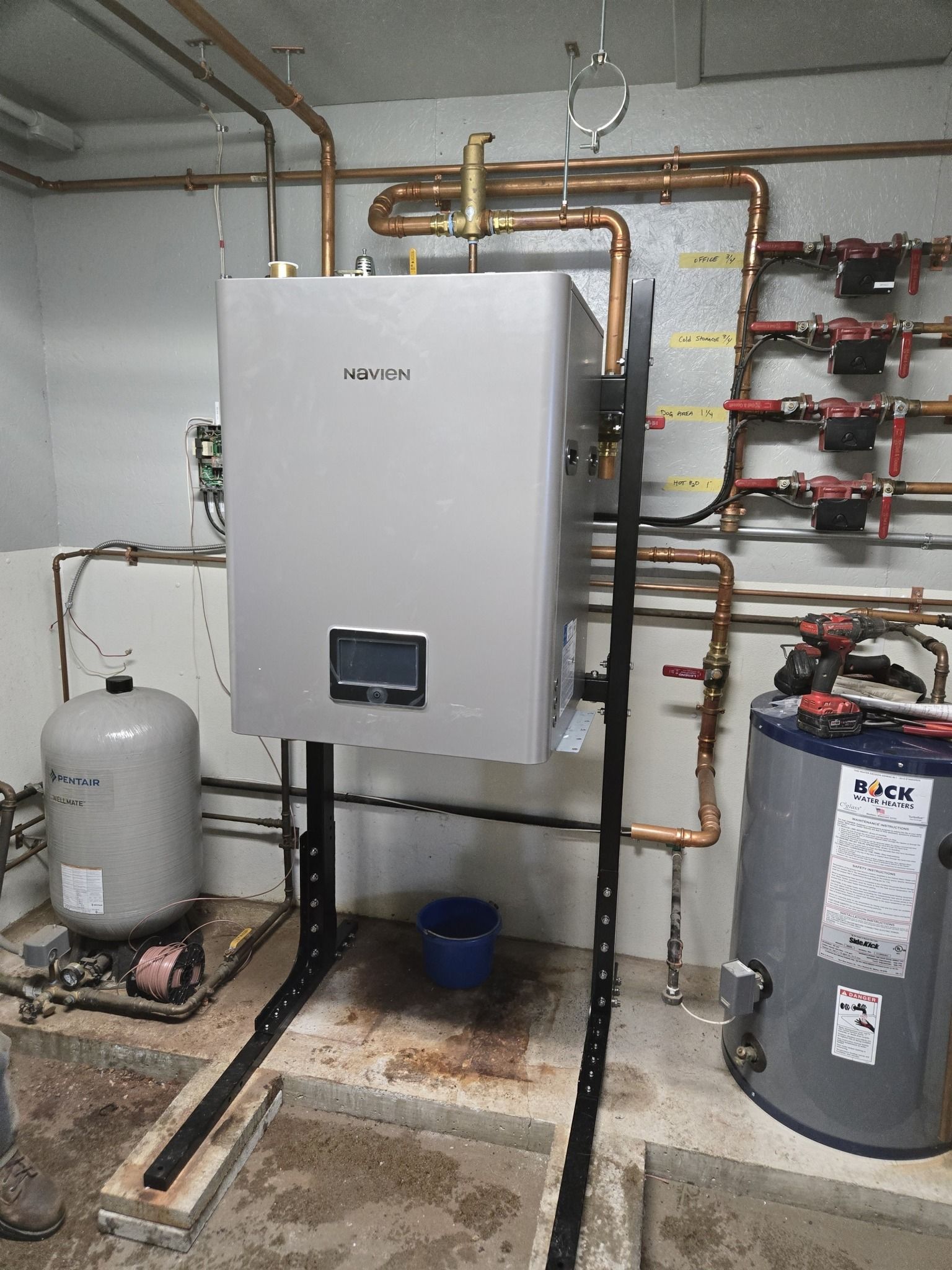 Boiler room with water heater, pipes, tanks, and floor drain in a basement utility area
