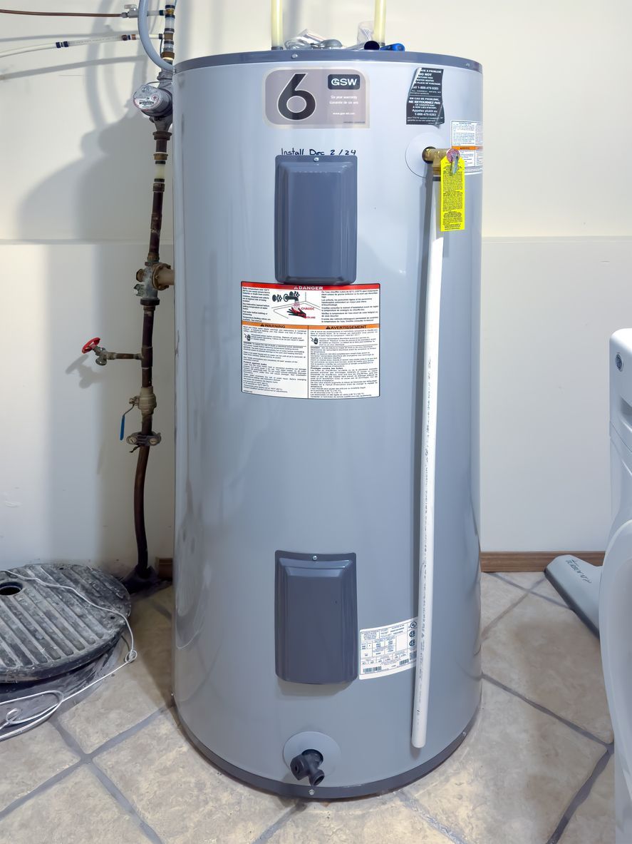 Gray water heater tank with labels, pipes, and gauge in a utility area