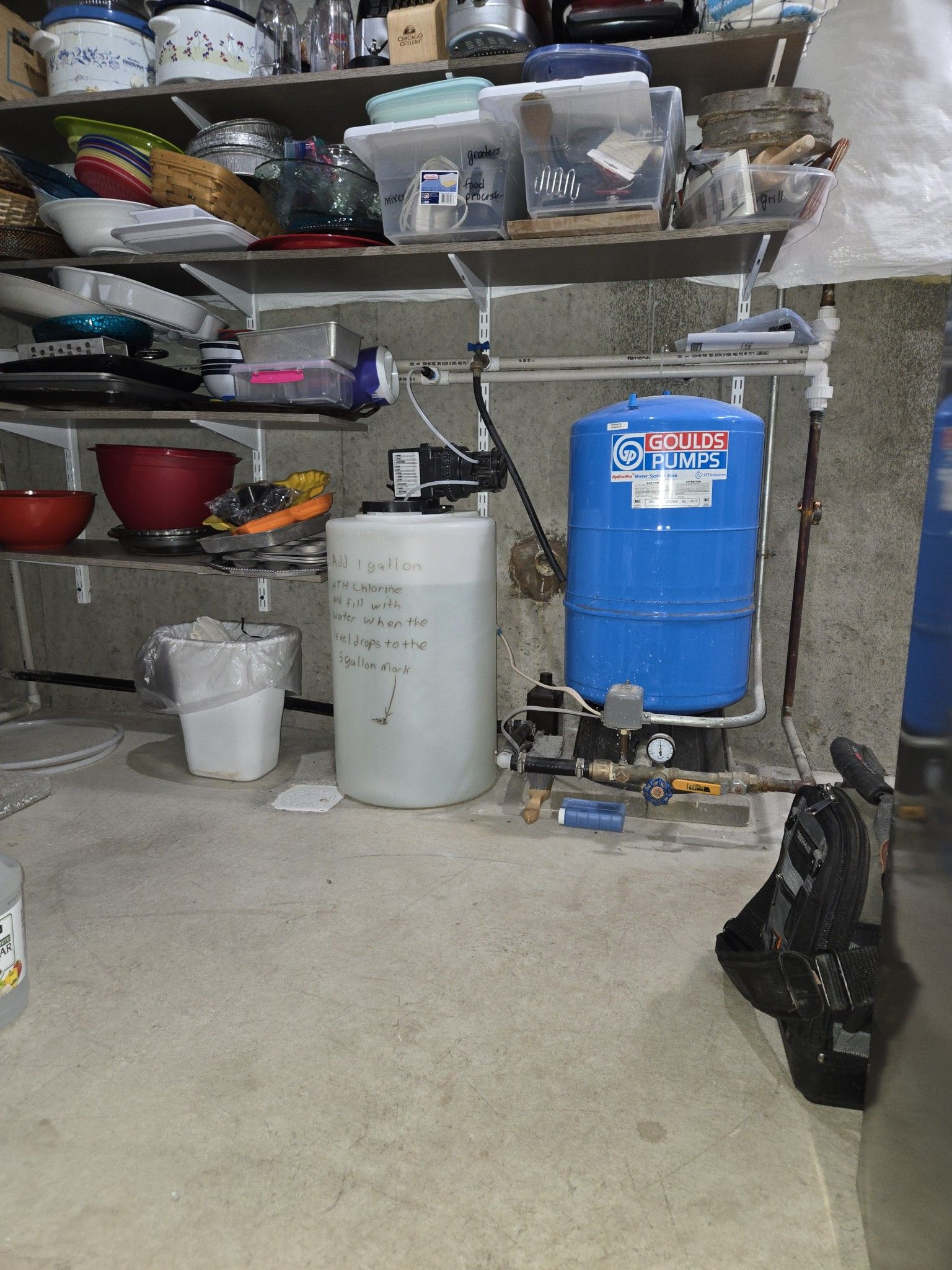 Basement storage area with shelves, buckets, and a blue water tank on a concrete floor.