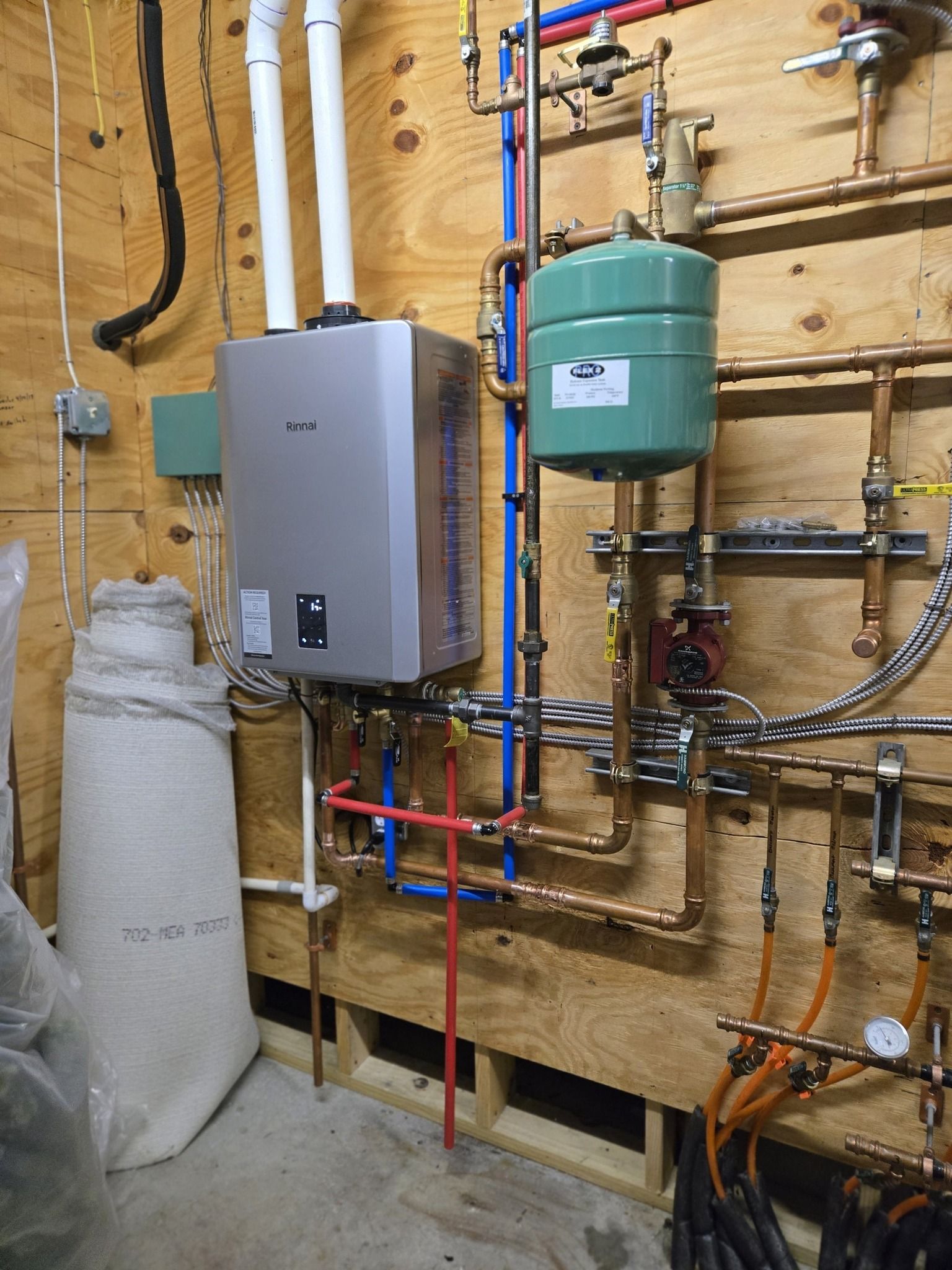 Wall-mounted water heater and plumbing pipes in a utility room with exposed wood framing.