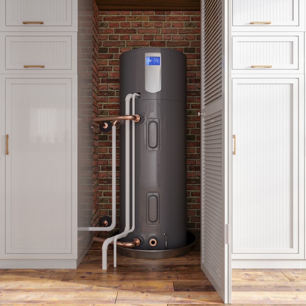 Water heater with exposed pipes in a brick alcove, flanked by white cabinets on a wooden floor.