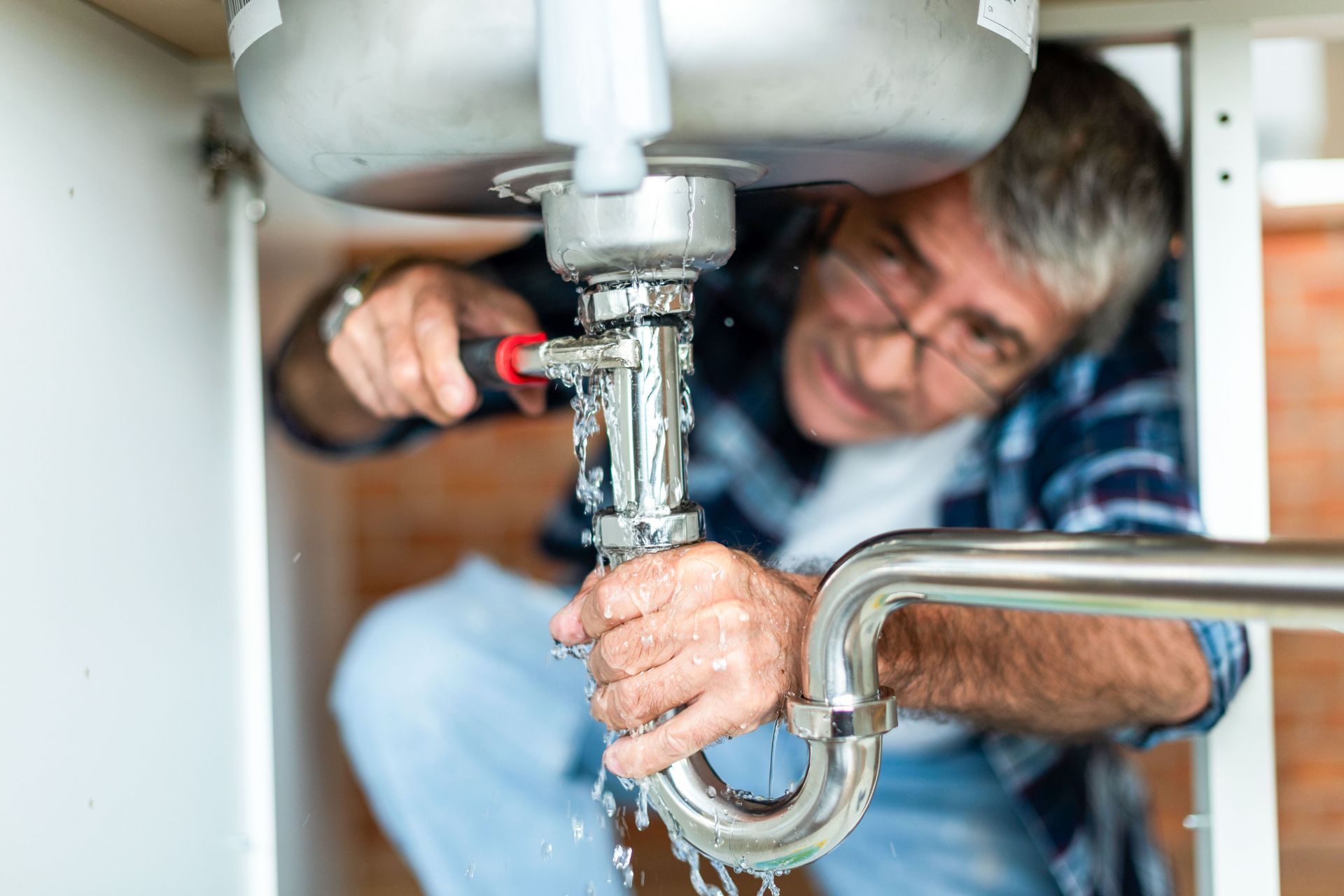 Plumber tightening a sink drain pipe under a bathroom sink with tools