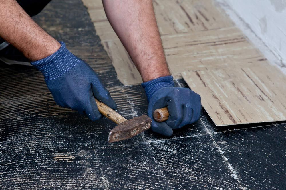 A Man is Hammering a Piece of Wood on the Floor — Maestro Tiling Services In Belconnen, ACT