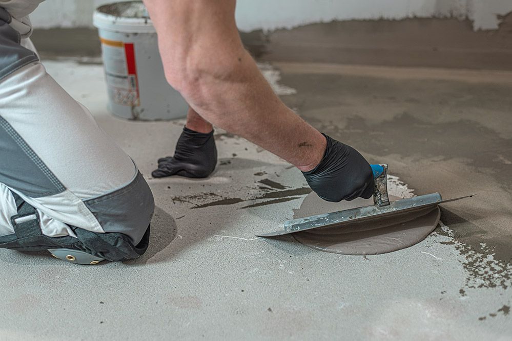 A Man is Laying Concrete on the Floor With a Trowel — Maestro Tiling Services In Gungahlin, ACT