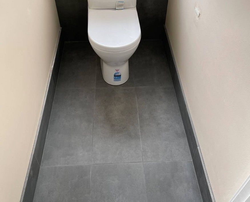 A Toilet is Sitting on a Tiled Floor in a Bathroom — Maestro Tiling Services In Latham, ACT
