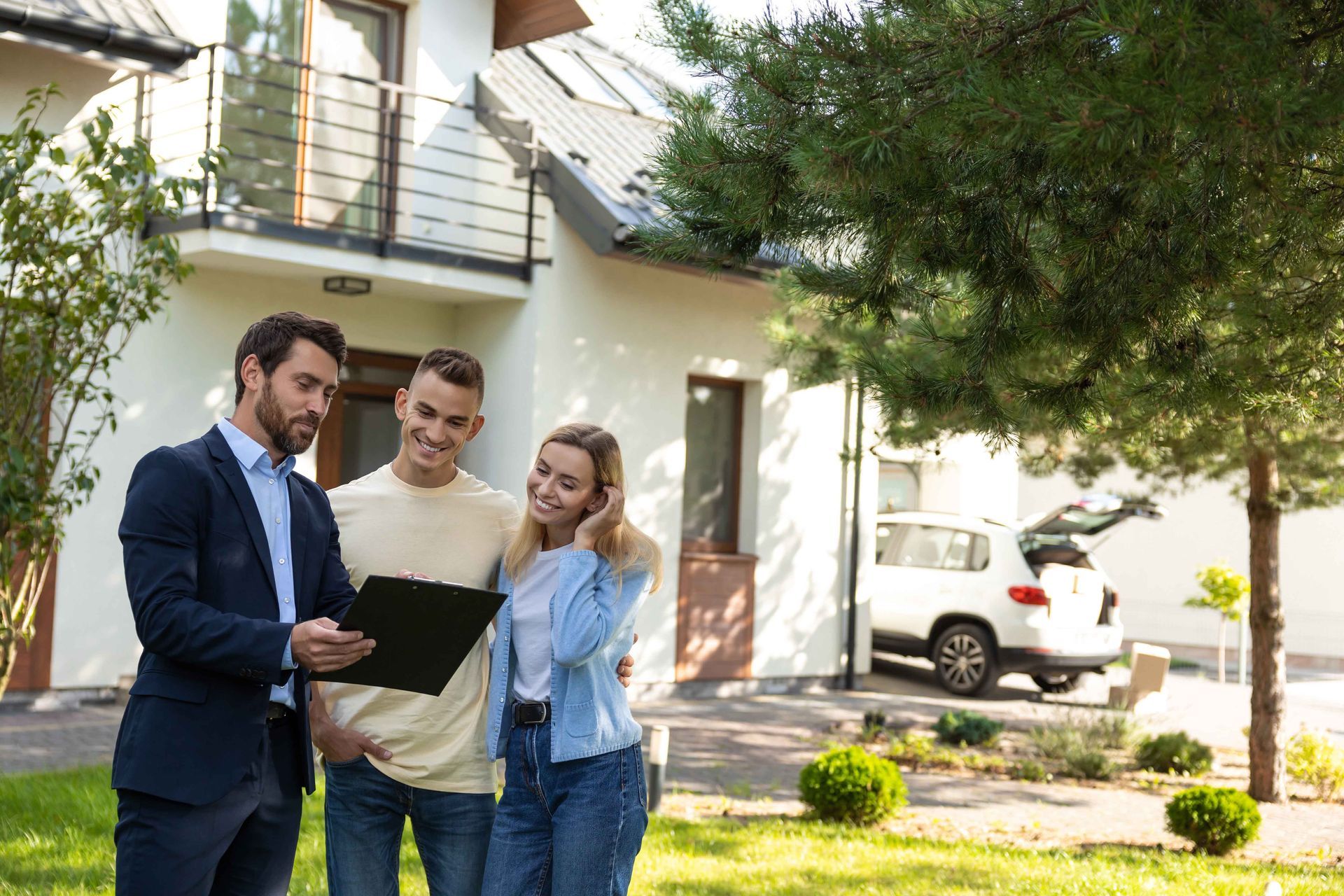 Un agent immobilier montre des documents à un couple devant une maison.