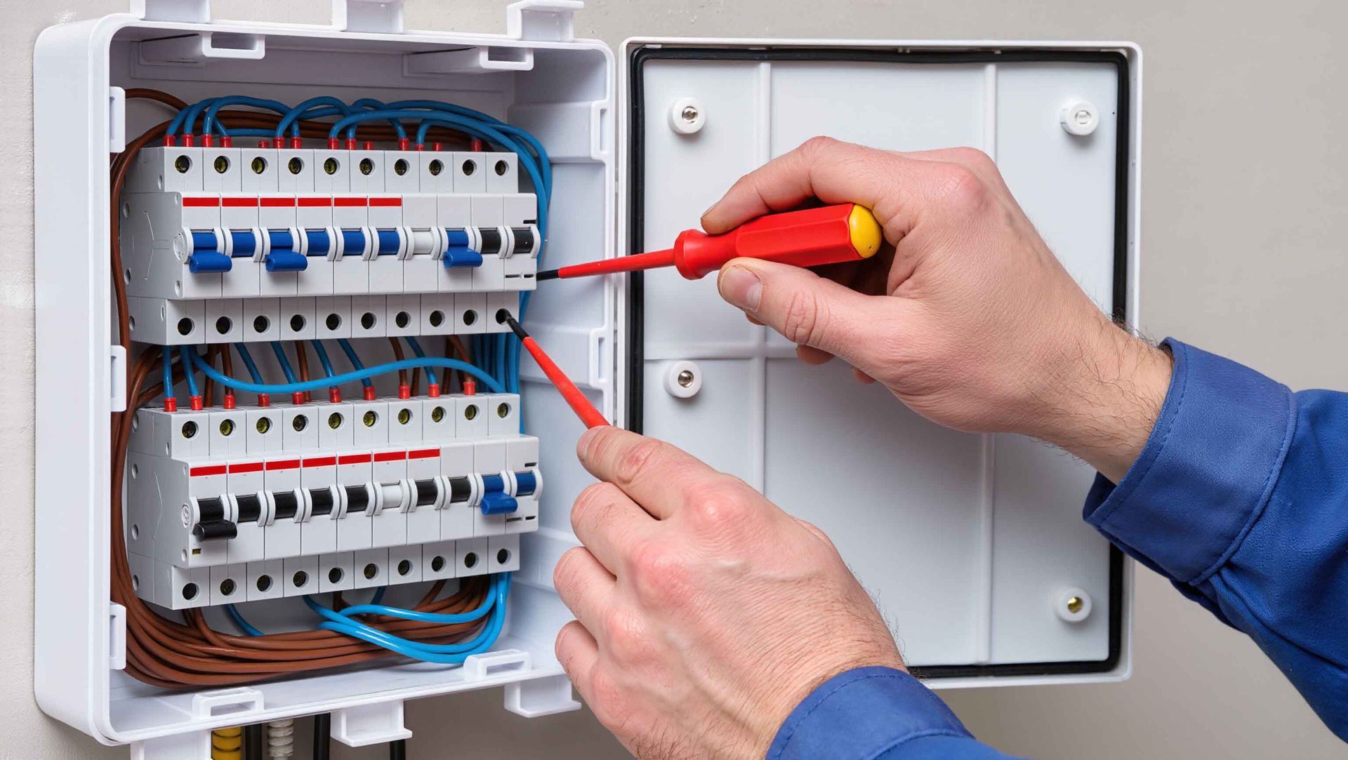 Un électricien utilise des tournevis sur un tableau électrique ouvert.