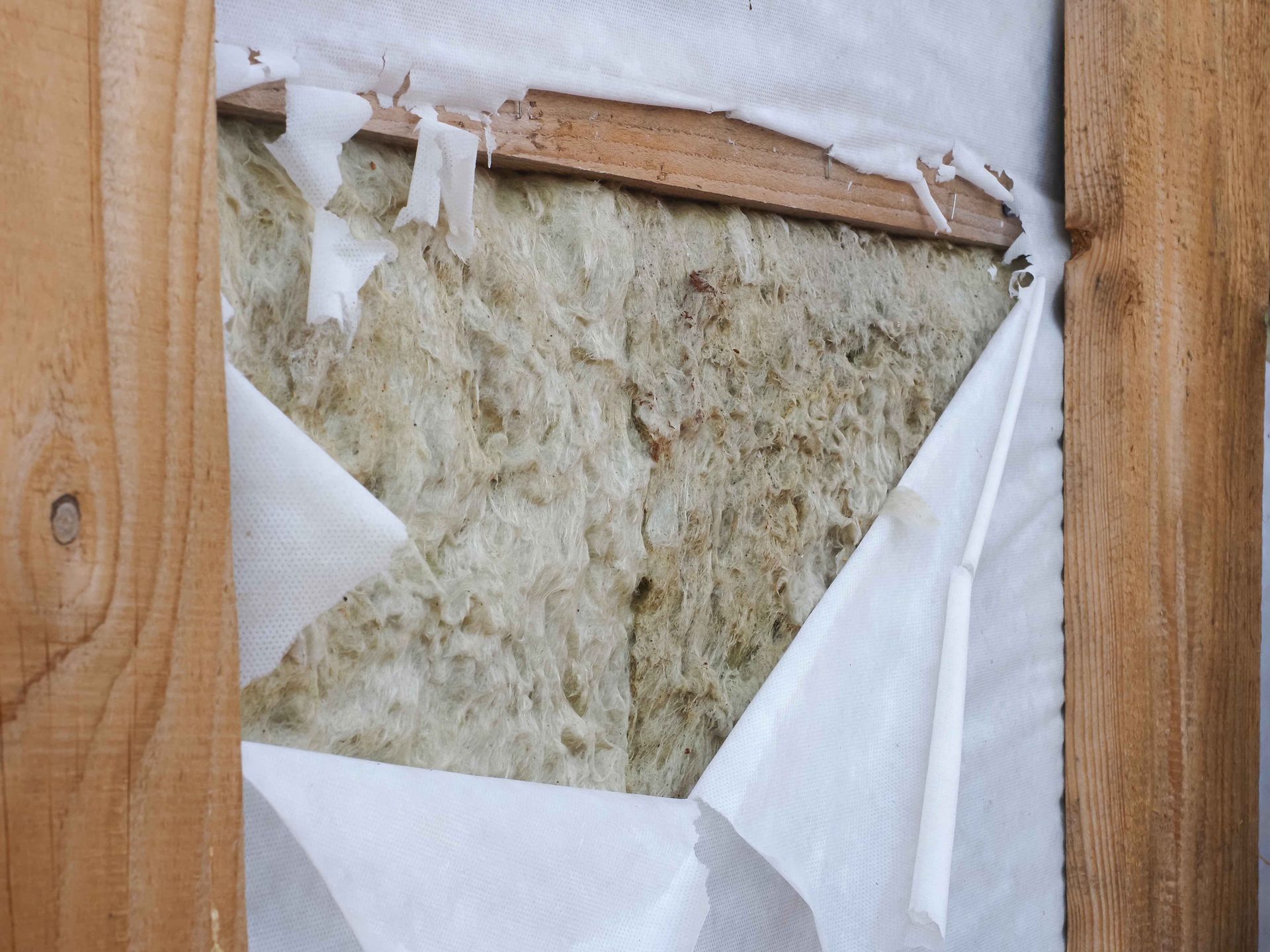 Un trou dans une structure en bois révèle un isolant enveloppé de papier blanc.