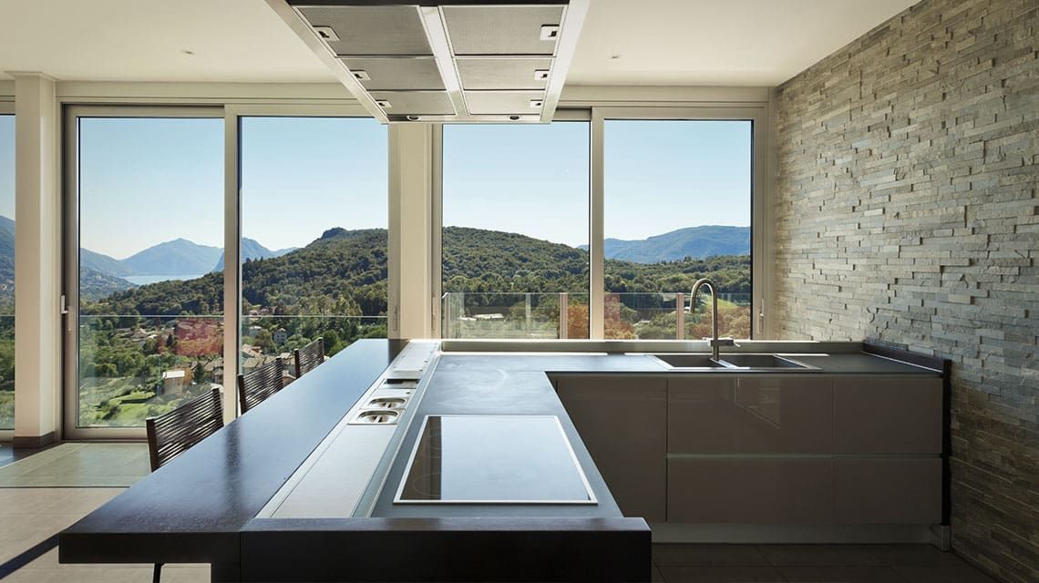 Cuisine moderne avec îlot central, grandes fenêtres, mur en pierre et appareils électroménagers intégrés.