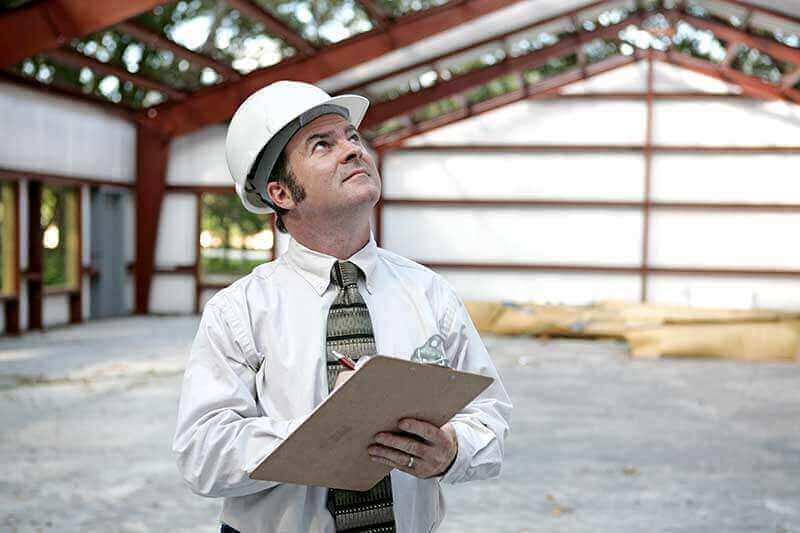 Un ouvrier du bâtiment, casque de chantier sur la tête, inspecte l'intérieur inachevé d'un bâtiment, un bloc-notes à la main.