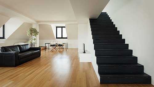 Espace de vie moderne et ouvert avec un escalier noir, un parquet et un canapé en cuir noir.