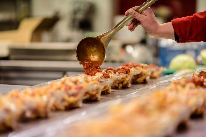 A person is pouring sauce into a tray of food with a ladle.
