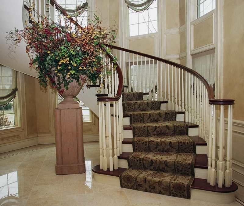 Curved staircase with carpet runner and large floral arrangement in a bright foyer
