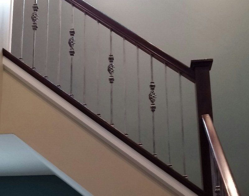 Wooden staircase railing with dark balusters and a beige wall indoors.
