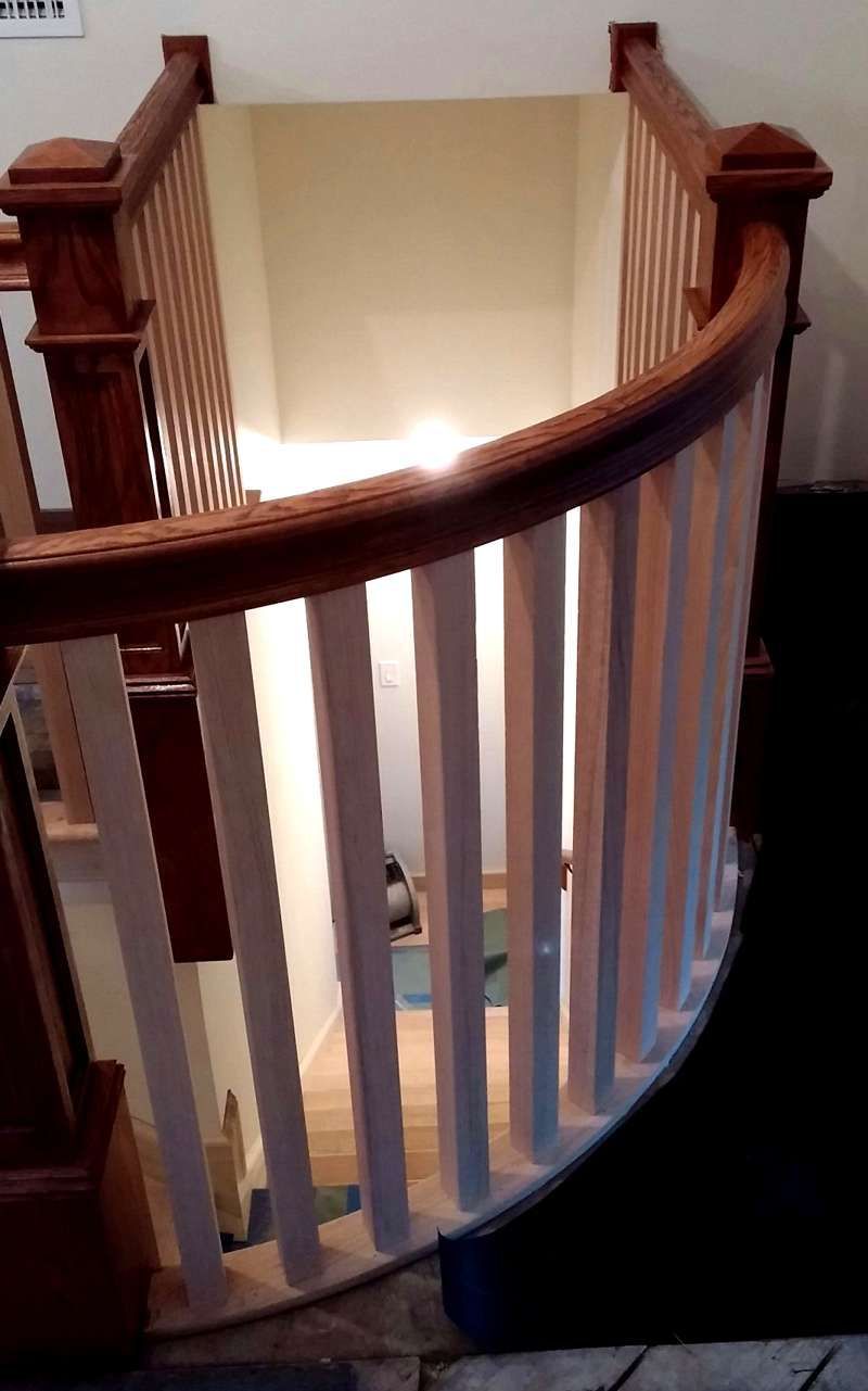 Curved wooden staircase with white balusters in a beige hallway, lit from below