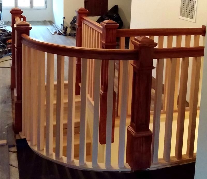 Curved wooden staircase railing with white balusters in an indoor hallway