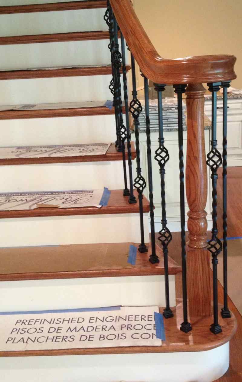 Wooden staircase with white risers, brown handrail, and ornate black iron balusters