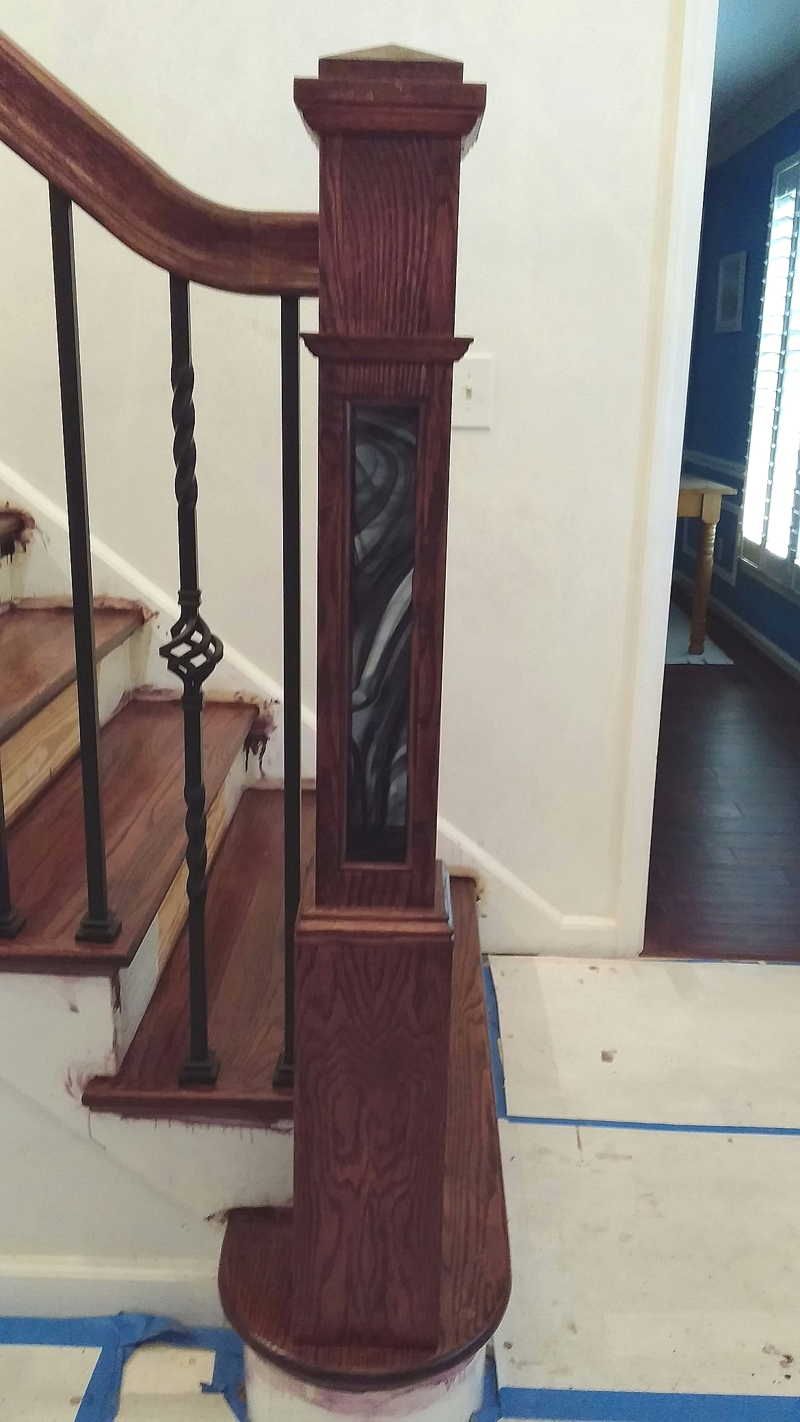 Wooden staircase newel post with ornate spiral detail beside a stair railing and doorway.