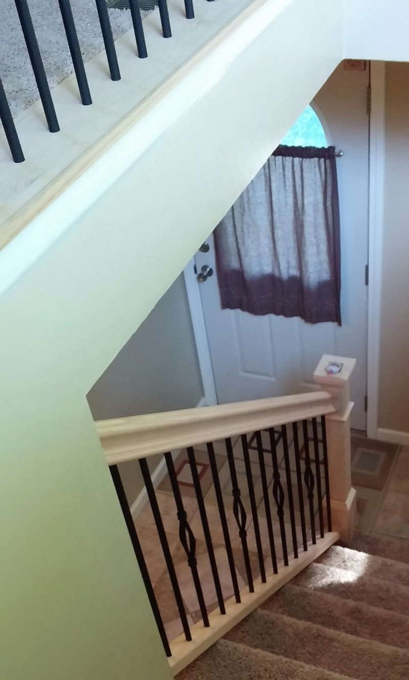Stairwell view with white walls, black railings, and a closed door with a curtain below.