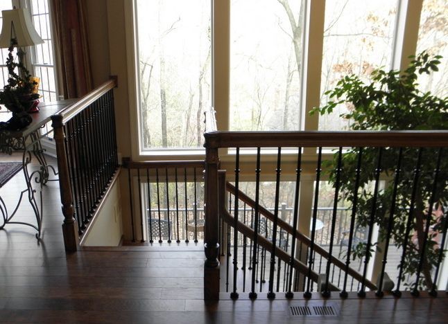 Staircase landing with dark wood railings beside tall windows and indoor plants in a bright foyer