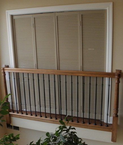 Closed beige window blinds behind a wooden railing inside a home hallway